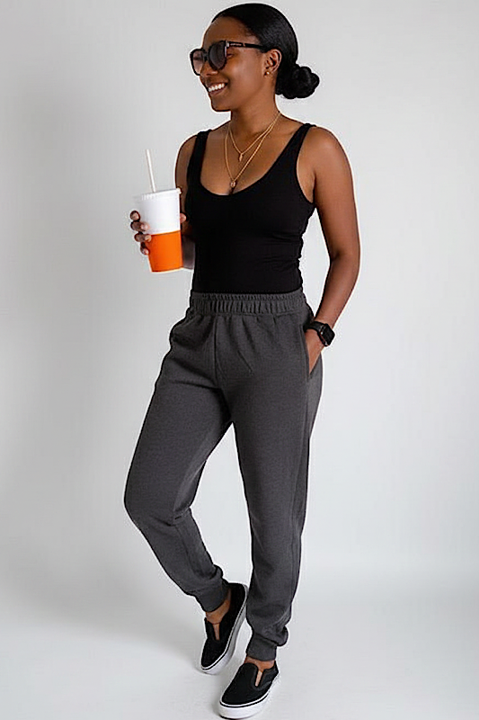 Woman wearing a black tank top and gray sweatpants, holding a drink.