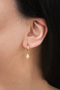 Gold huggie hoop earrings with dangling charm shown on model with pulled back hair